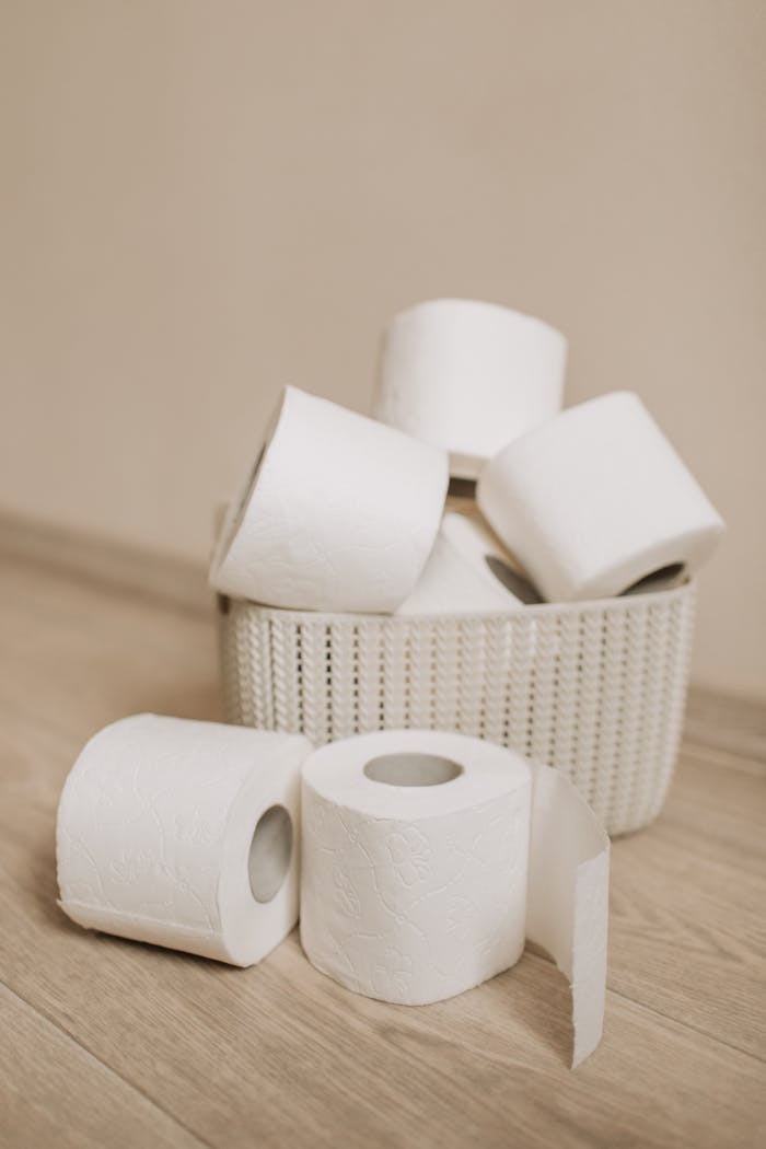 A collection of toilet paper rolls stacked in a woven basket on a wooden floor.