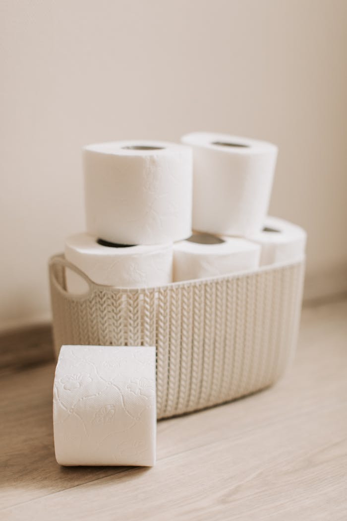 A woven basket filled with stacked white toilet paper rolls on a light wooden floor, perfect for hygiene and cleaning themes.