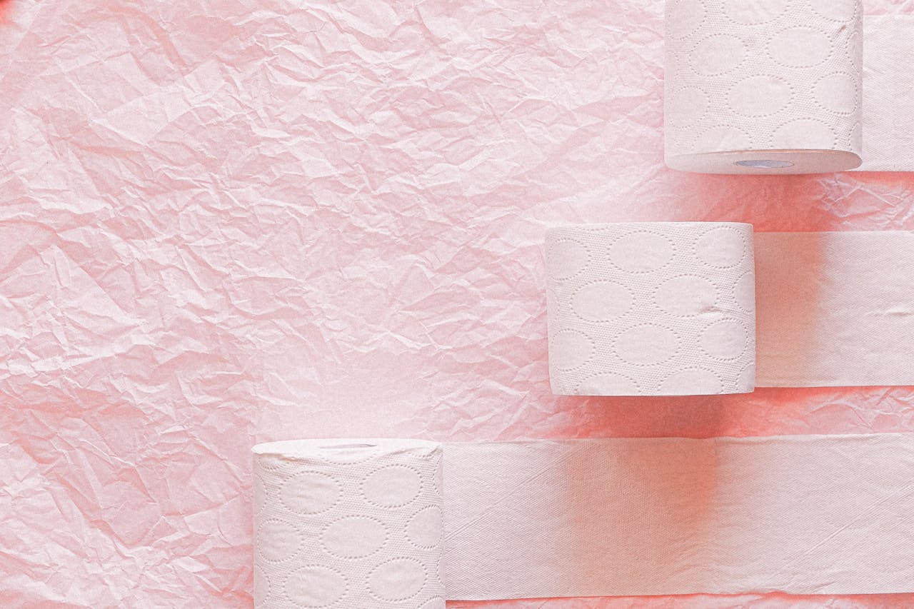 Toilet paper rolls arranged on a pink textured background for a clean, minimalist look.