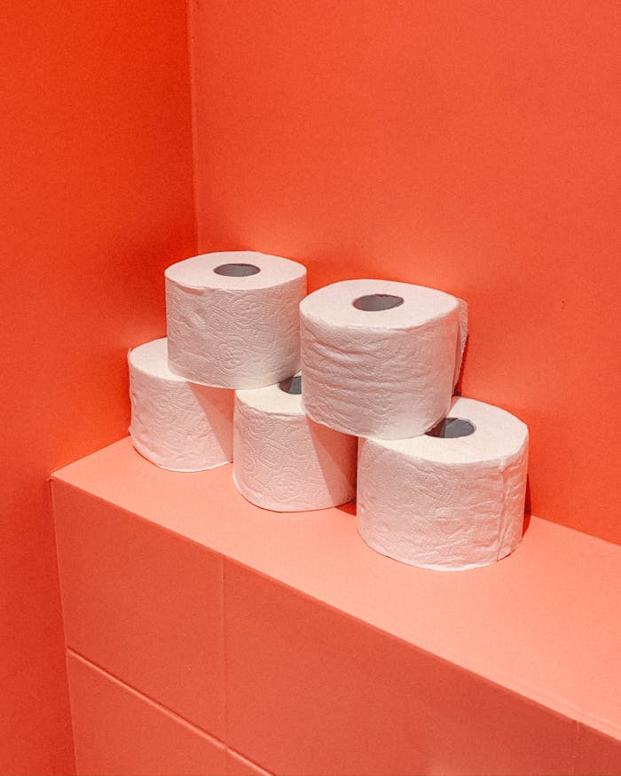 Close-up image of stacked toilet paper rolls on a pink colored bathroom wall.